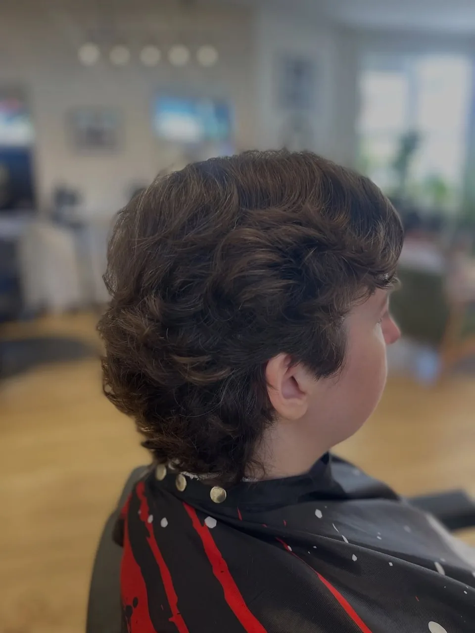 A curly mullet in profile — short and textured through the top, trailing longer at the nape.